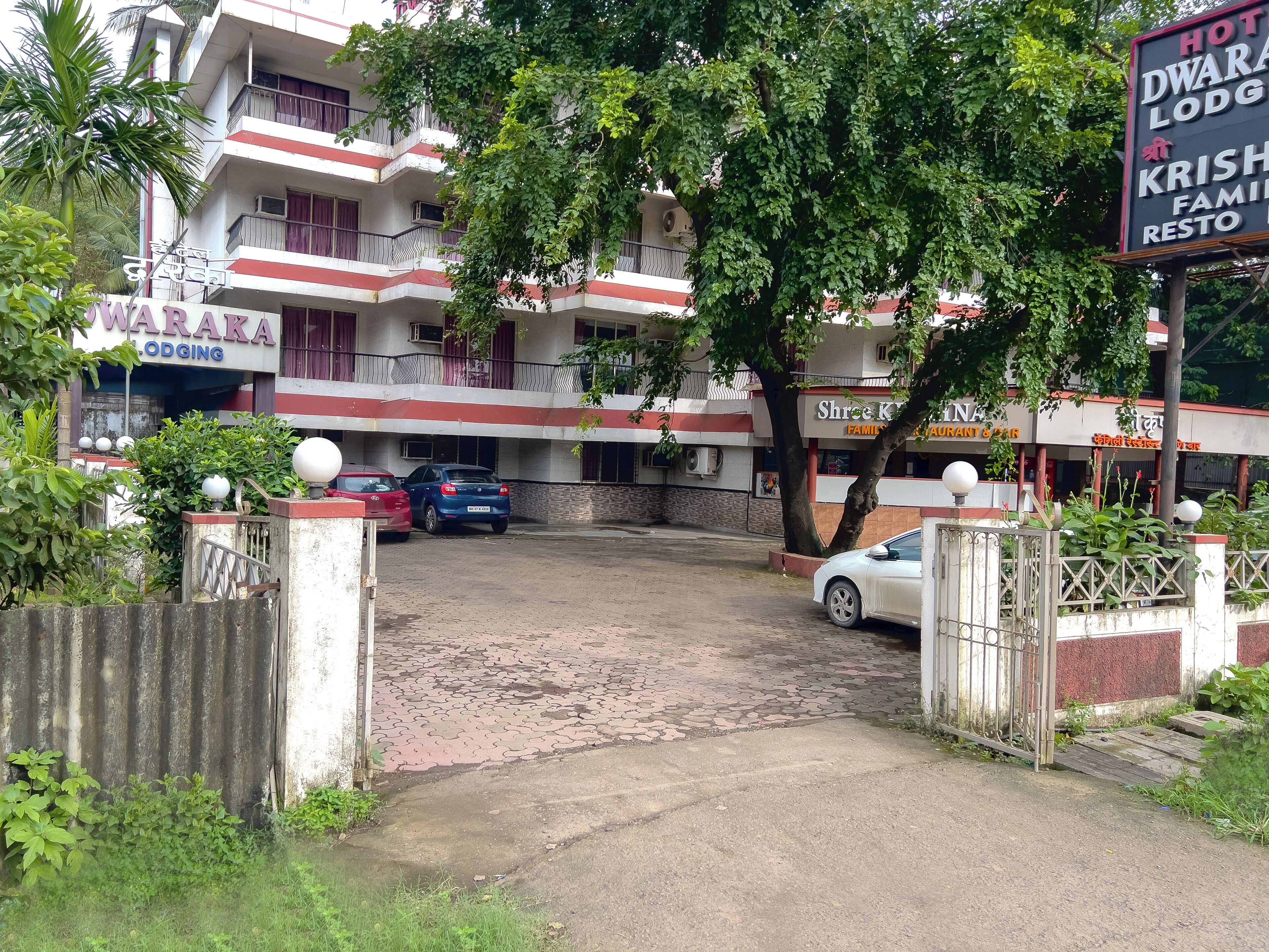 A hotel with a gated entrance, parked cars, and a signboard advertising services.