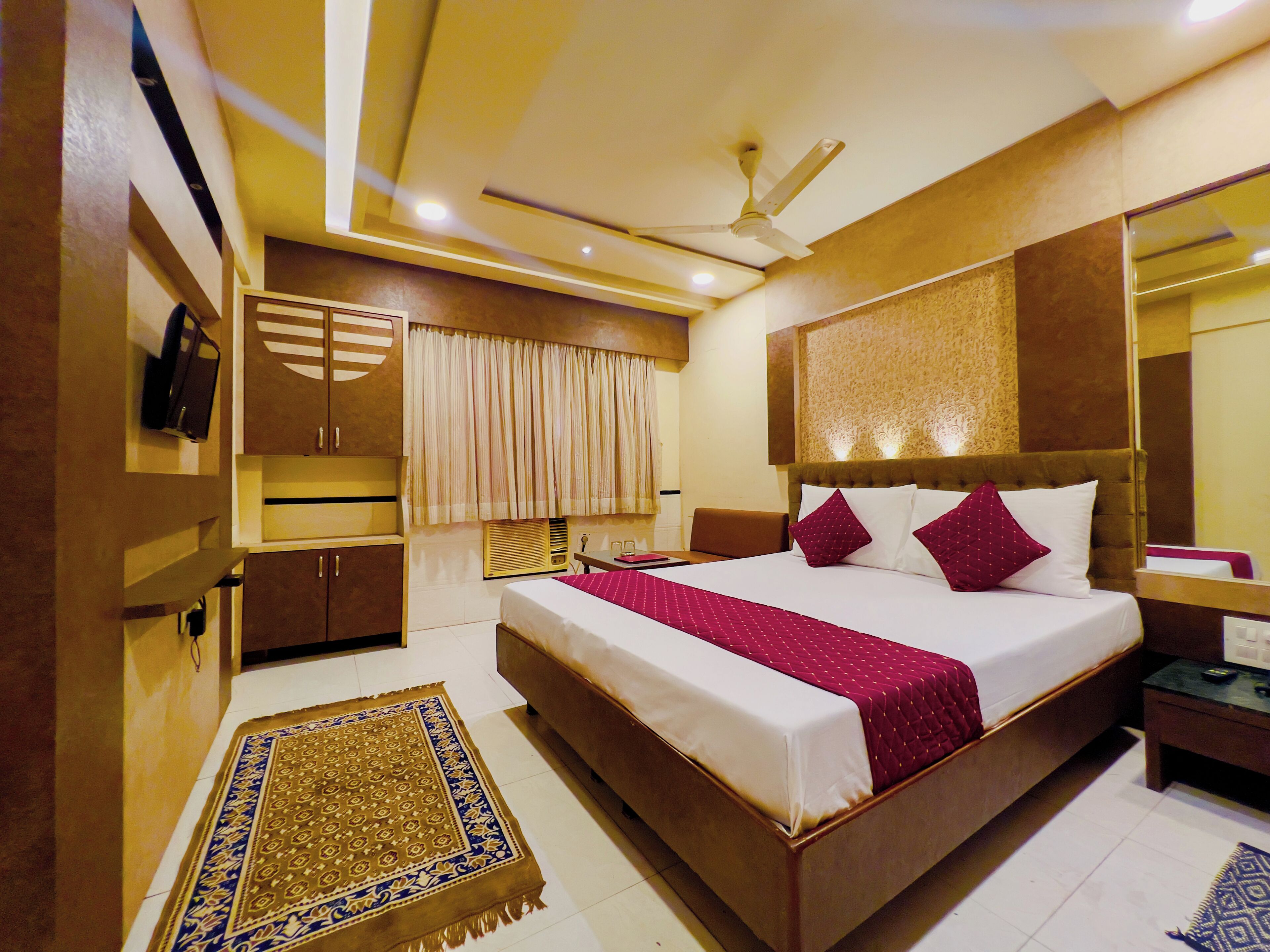 A hotel room with a large bed, a ceiling fan, a TV, and a minibar.