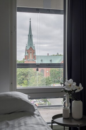 Ein Hotelzimmer mit einem großen Fenster, das Blick auf eine Kirche mit einem hohen Spitzenturm und ein Backsteingebäude bietet.