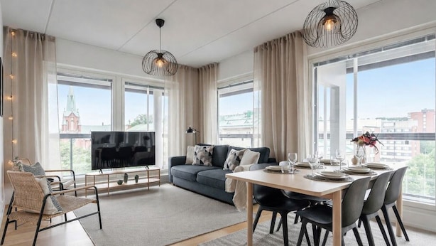 A modern living room with a sofa, TV, dining table, and large windows. - Modern 2BR Apartment with Sauna & Large Balcony (Tampere)