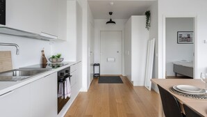 A modern kitchen with white cabinets, a stainless steel sink, and a small dining area with a table set for two. - Modern 2BR Apartment with Sauna & Large Balcony (Tampere)