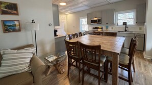 A modern kitchen with white cabinets, a large wooden dining table, and a built-in oven. - 7 mins to Acadia and walk to town! (Southwest Harbor)