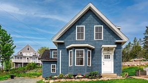 A two-story house with a gabled roof, a front porch, and a small garden area with rocks and plants. - 7 mins to Acadia and walk to town! (Southwest Harbor)