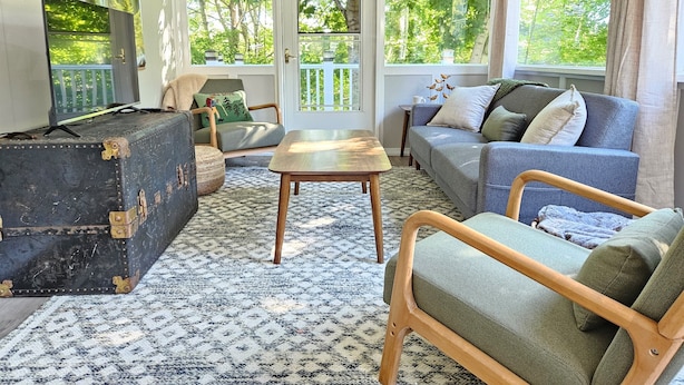 A cozy living room with a sofa, armchair, and a table. There's a suitcase and a television on a stand. - 7 mins to Acadia and walk to town! (Southwest Harbor)
