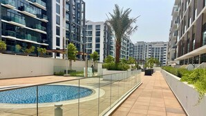 A modern residential building with a rooftop pool, glass railings, and greenery.