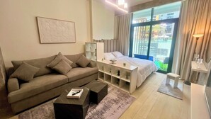 A modern hotel room with a sofa, a bed, a small table, and a large window with curtains.