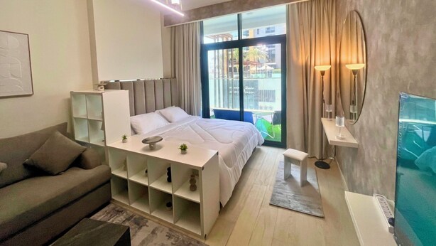 A modern hotel room with a large bed, a sofa, a desk, and a TV.