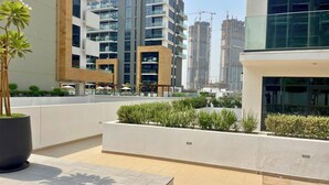 A modern outdoor area with a flat terrace, potted plants, and a view of high-rise buildings in the background.
