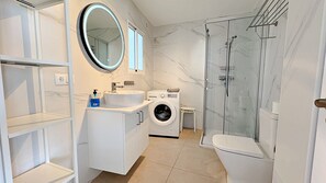Ein modernes Badezimmer mit Waschmaschine, Waschbecken, Spiegel und Duschkabine aus Glas.