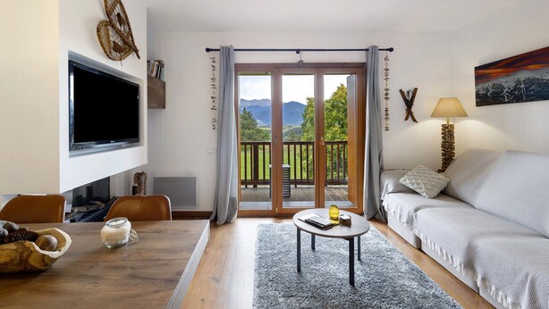 A living room with a TV, sofa, table, and a view of mountains through a balcony. - Unique Apartment in Font Romeu (Font-Romeu)