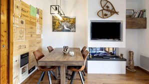 A dining area with a wooden table and chairs, a mounted TV, and a wall with wooden crates and a painting. - Unique Apartment in Font Romeu (Font-Romeu)