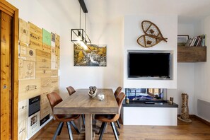 Un comedor con una mesa y sillas de madera, un televisor montado, y una pared con cajas de madera y un cuadro.