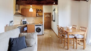 A compact kitchen with a washing machine, wooden cabinets, and a dining area with a table and chairs. - Ideal Apartment in Osséja (Osséja)