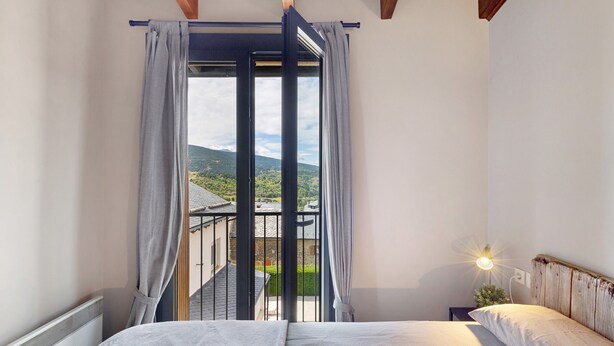 A bedroom with a bed, a nightstand with a lamp, and a view of a balcony with a railing. - Ideal Apartment in Osséja (Osséja)
