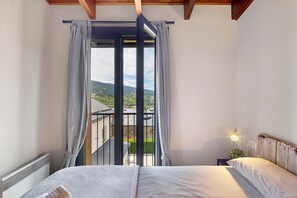 A bedroom with a bed, a nightstand with a lamp, and a view of a balcony with a railing. - Ideal Apartment in Osséja (Osséja)