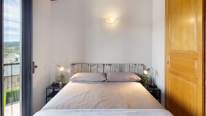 A bedroom with a bed, two bedside tables with lamps, a wooden ceiling, and a view through a glass door. - Ideal Apartment in Osséja (Osséja)
