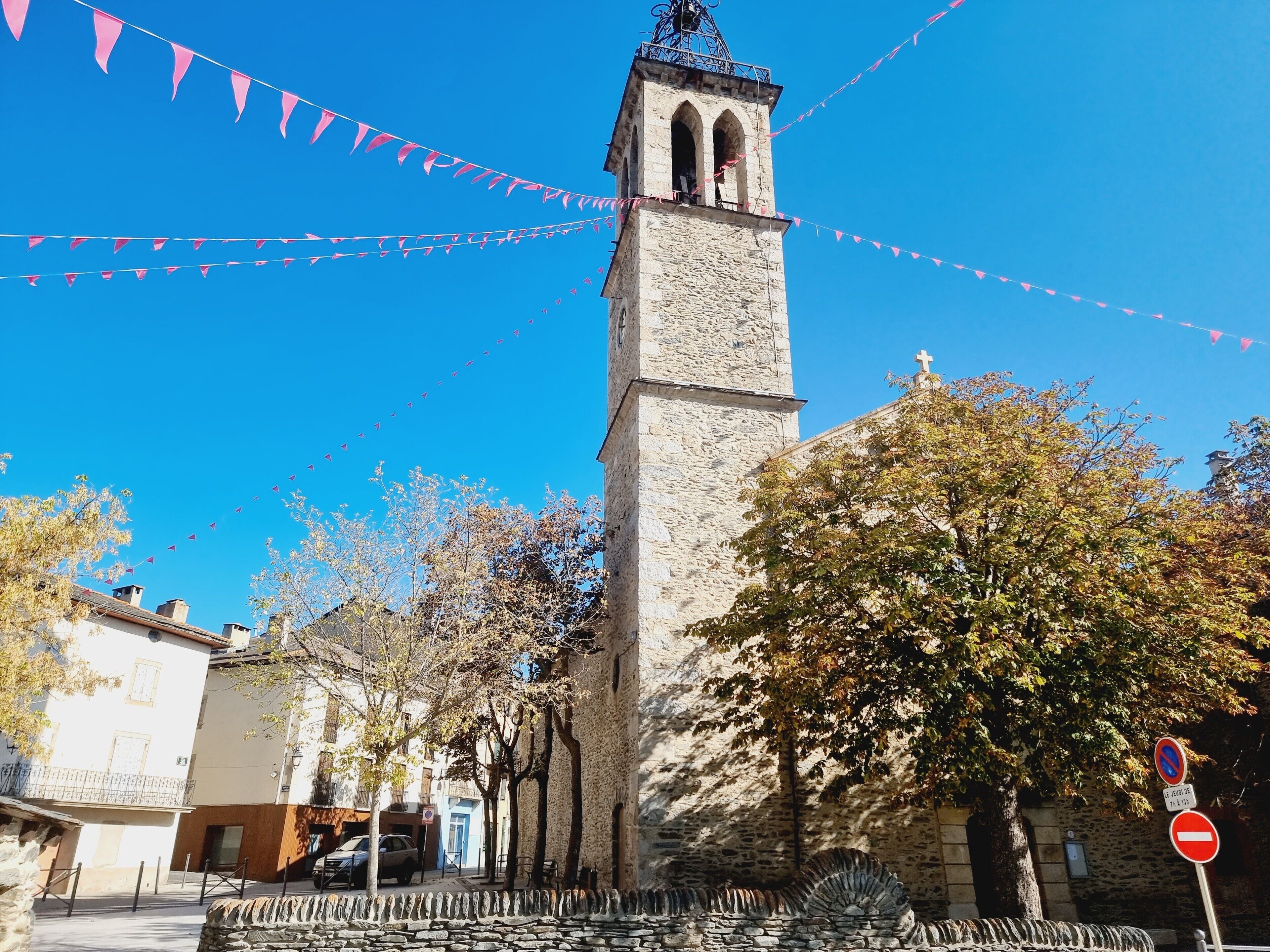 Una torre in pietra con un orologio, circondata da alberi e edifici.