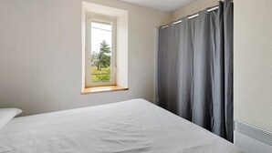 Une chambre avec un lit simple, une fenêtre donnant sur un paysage verdoyant et un rideau gris.
