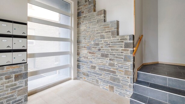 Un escalier avec des marches en pierre et une rampe en bois, une rangée de casiers et une porte en verre.