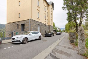 A building with a stone facade and a flat roof, adjacent to a road with parked cars.