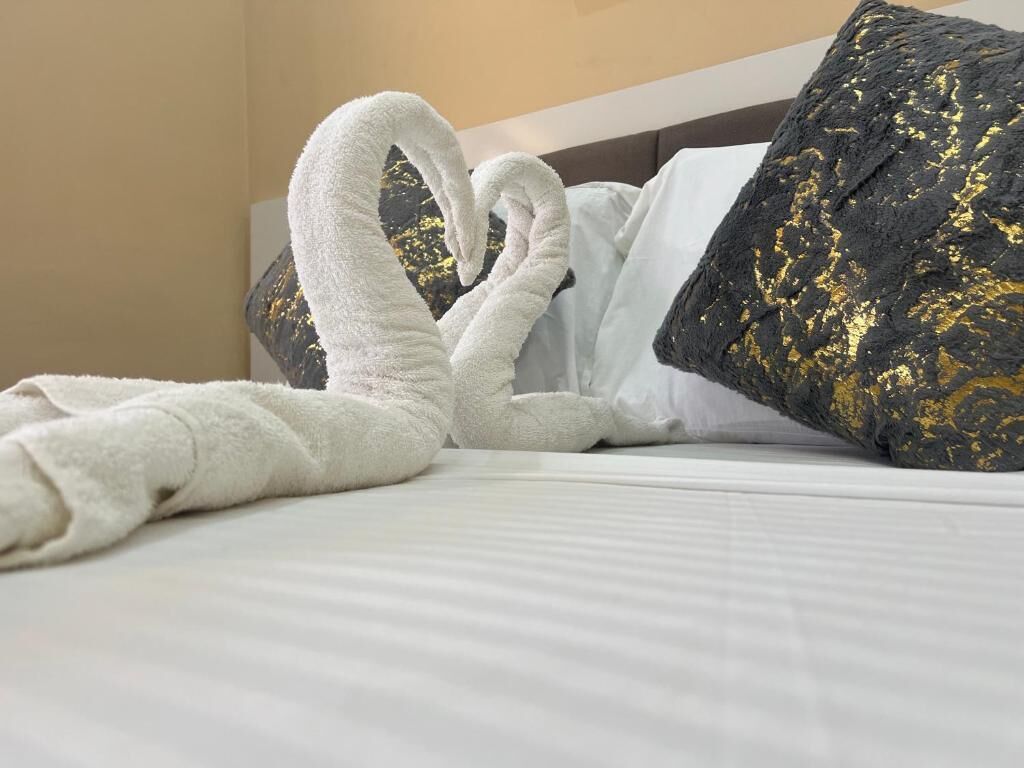 A bed with white linens and a black pillow with gold patterns.