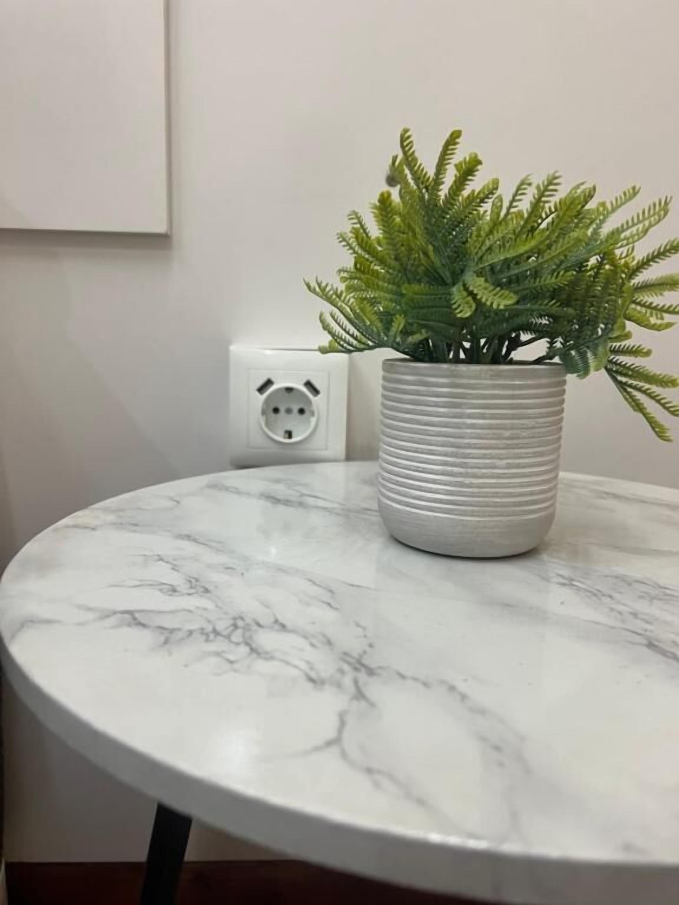Una mesa redonda de mármol con una heleadera en maceta.