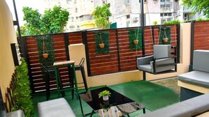 Een klein terras met een tafel en stoelen, een hangplant en een groen tapijt.