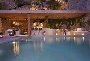 A pool area with a bar and seating, surrounded by stone walls and greenery.