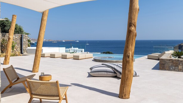 Un espace aménagé au bord de la piscine, avec des chaises longues, un parasol et une vue sur la mer.
