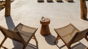 Un espace extérieur aménagé, abrité et doté de fauteuils confortables et d’une petite table, offrant une vue sur une piscine et un paysage rocheux.