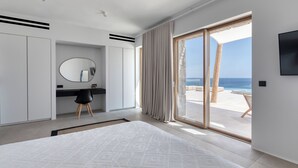 Une chambre moderne avec un grand lit, un bureau et une vue sur la plage, visible à travers la porte-fenêtre coulissante.
