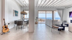 Un vaste espace de vie avec une grande fenêtre donnant sur la mer, un coin repas agrémenté d’une guitare et un coin salon confortable avec un téléviseur.