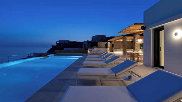 A modern outdoor pool area with lounge chairs and a dining area, overlooking a body of water.