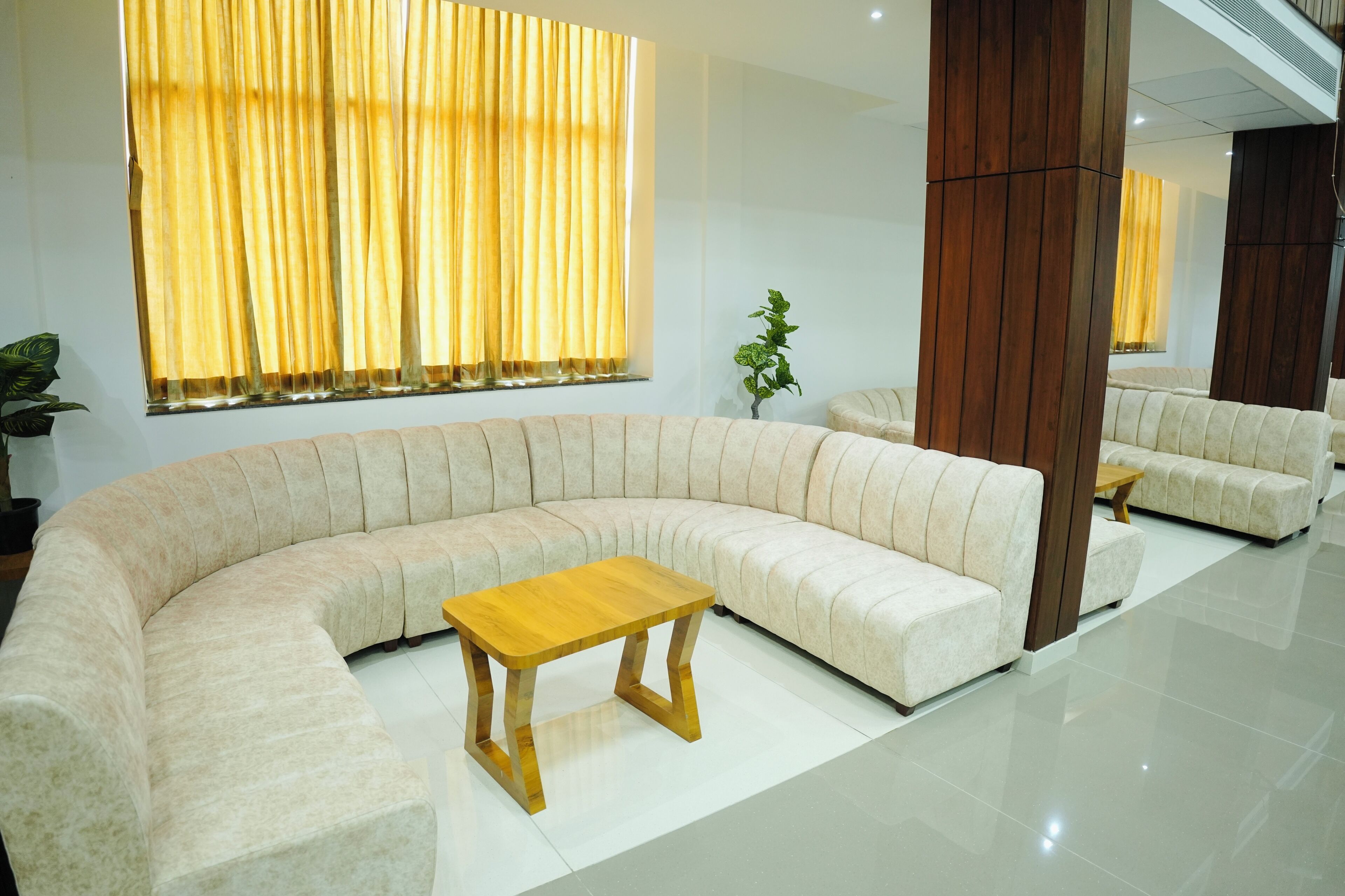 A modern living room with a curved beige sofa, a wooden coffee table, and a large window with yellow curtains.