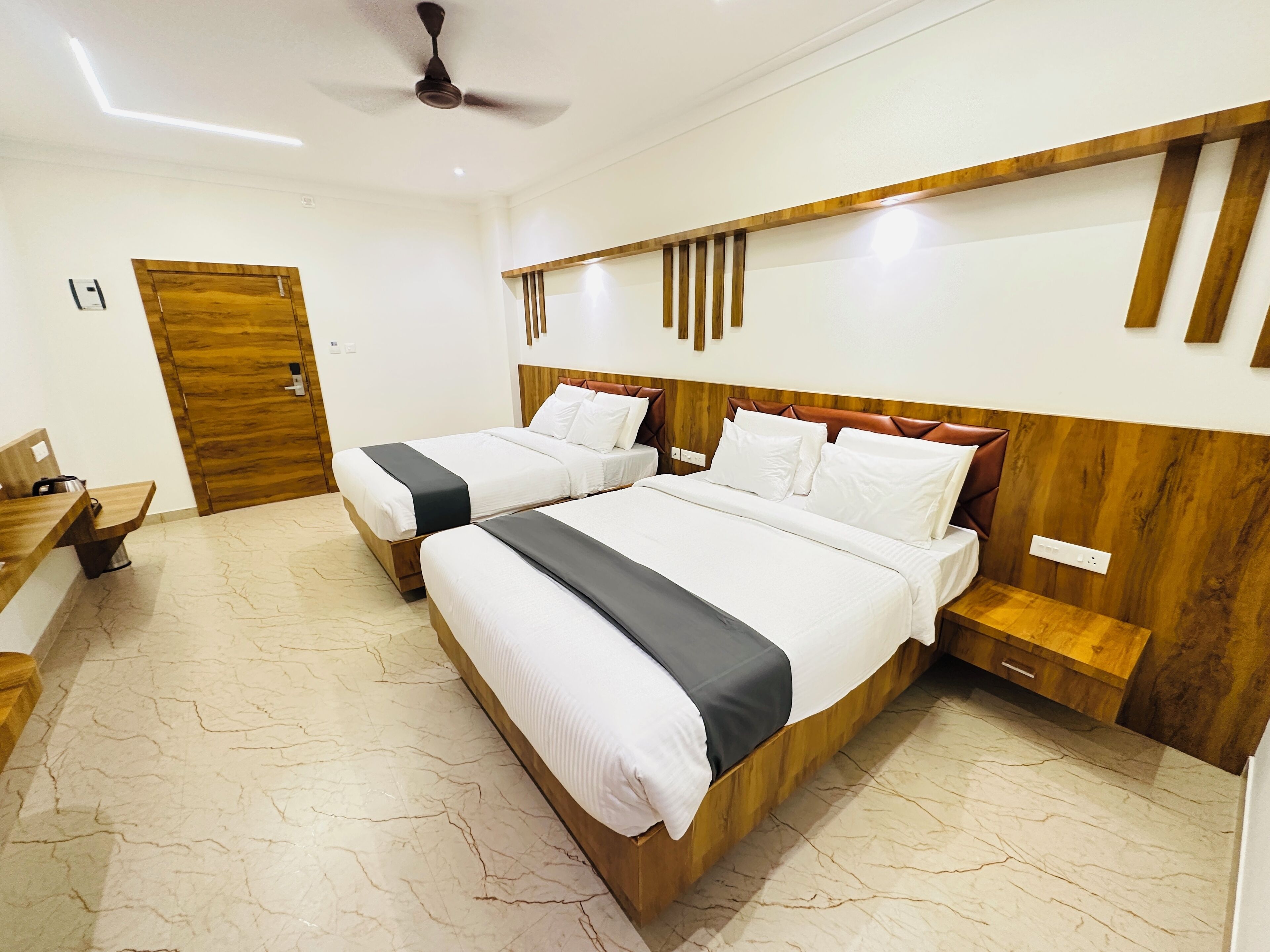 A hotel room with two beds, a wooden headboard, a small bedside table, a desk, and a door.
