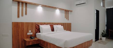 A modern bedroom with a wooden headboard, a bedside table with a phone, and a potted plant.