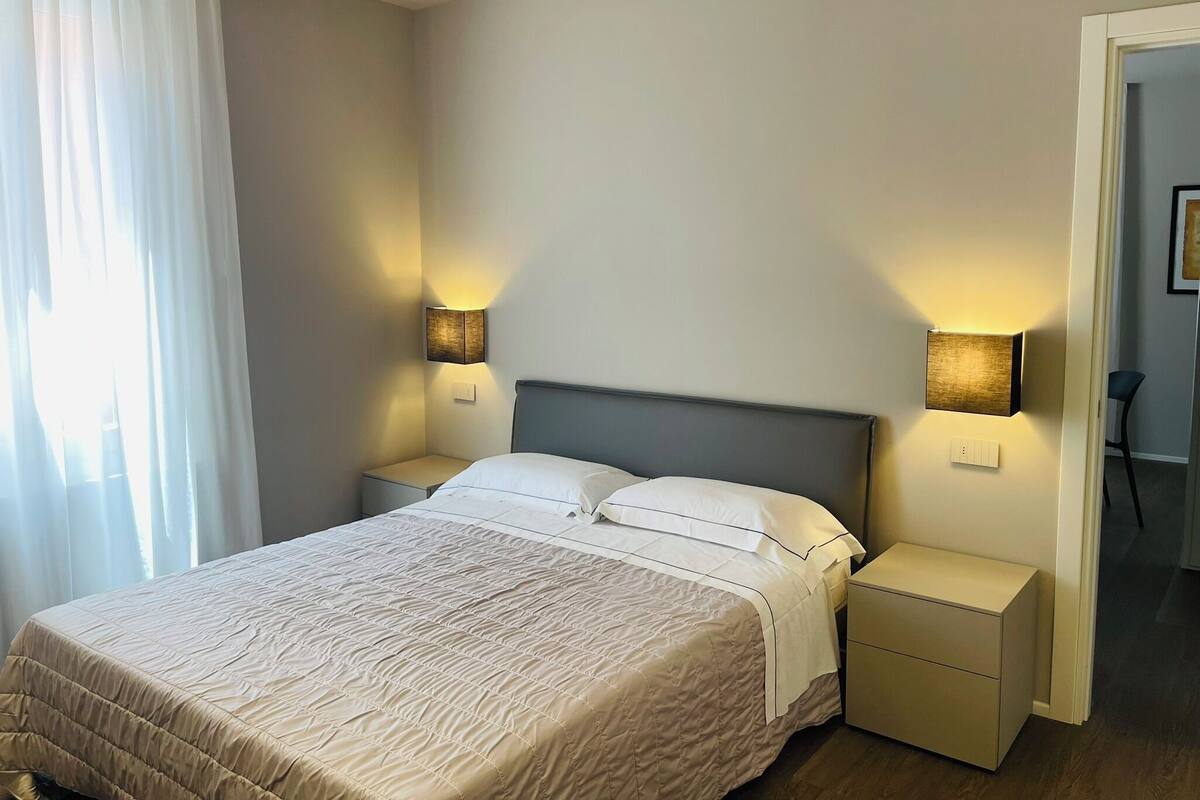 A hotel room with a bed, two bedside tables, and two wall-mounted lamps.