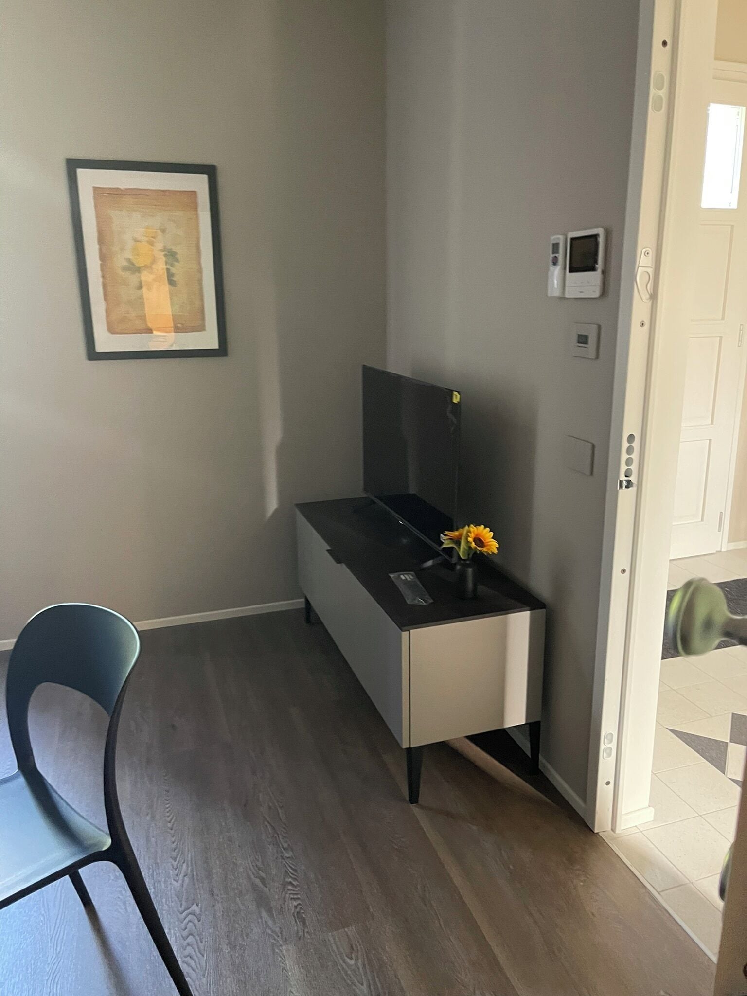 Une pièce avec un bureau, une chaise, un tableau encadré au mur et une porte dotée d’une poignée.