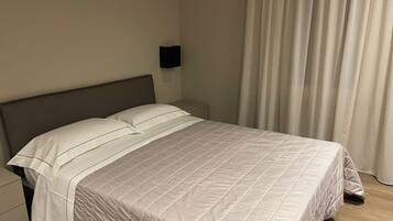 Una cama bien hecha con cubrecama acolchado, una mesita de noche y una lámpara fijada a la pared.
