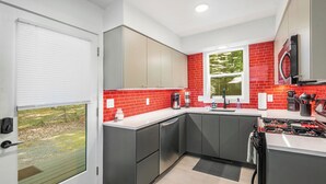A modern kitchen with grey cabinets, a red-tiled backsplash, and a large window providing natural light. - 3 Bedroom, 1.5 Bath Chalet minutes from Hamlin Lake. Sleeps 8 (Ludington)