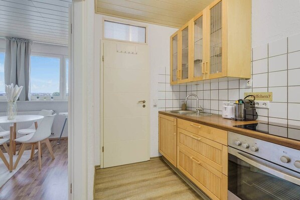 Een koelkast, een oven, een kookplaat, kookgerei, borden en bestek