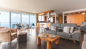 A spacious living area with a grey sofa, wooden coffee table, wicker furniture, and a view of the sea through large windows. - Cape View Villa by Atlantic Holiday (Calheta)