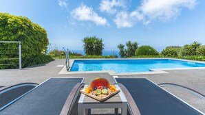 A poolside area with a table set with fruit and a view of the ocean. - Cape View Villa by Atlantic Holiday (Calheta)
