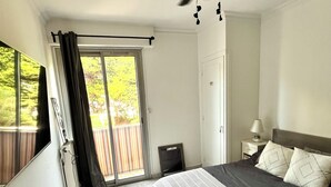 A bedroom with a bed, a ceiling fan, a window with curtains, a nightstand, and a view of the outdoors. - La Casa de la Rosa (Mandelieu-la-Napoule)