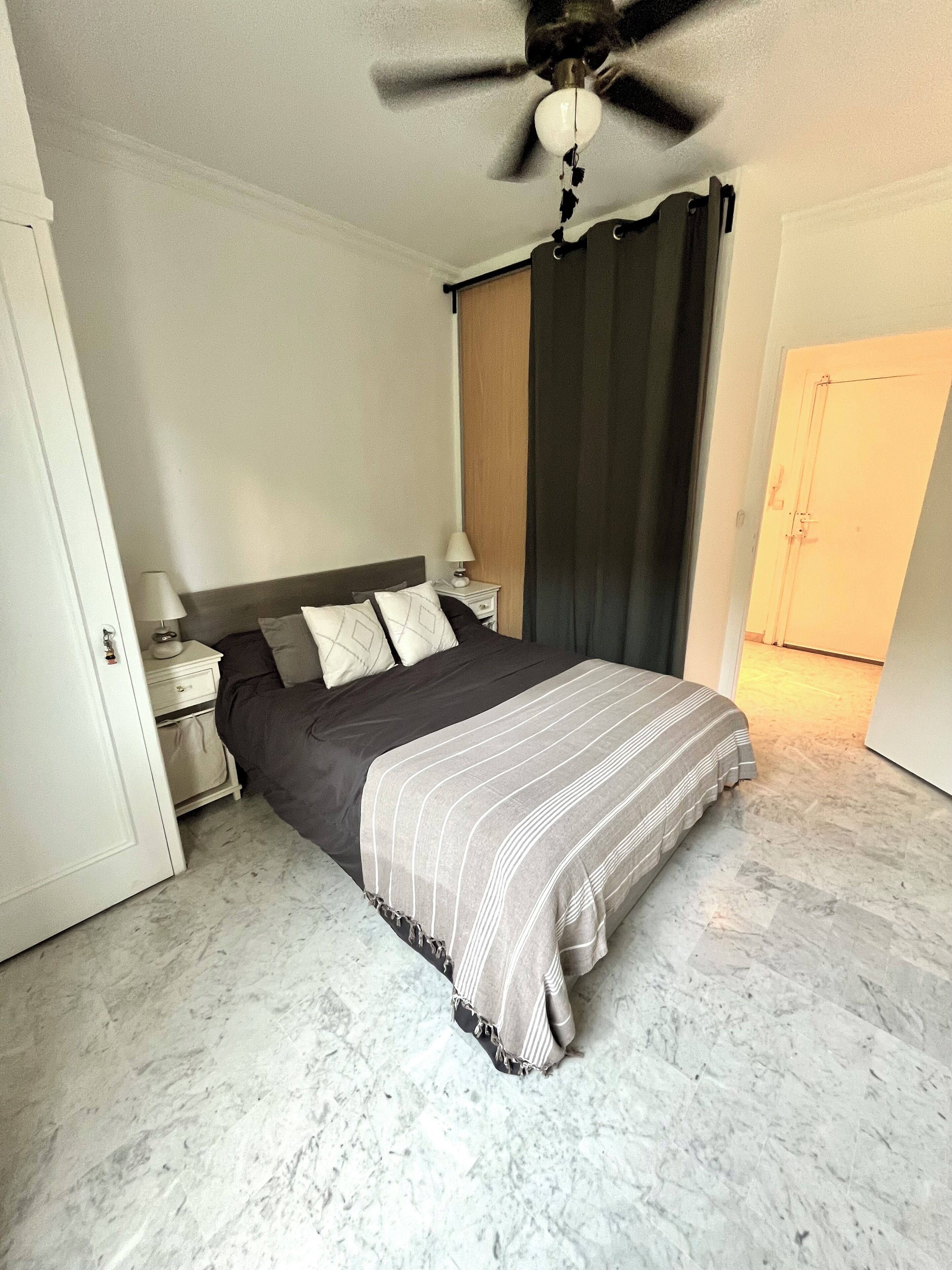 Een slaapkamer met een bed, nachtkastje, plafondventilator en een deur.