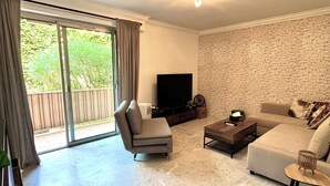 A spacious living room with a large sliding glass door leading to a balcony, a flat-screen TV, a sofa, a coffee table, and a stone wall. - La Casa de la Rosa (Mandelieu-la-Napoule)