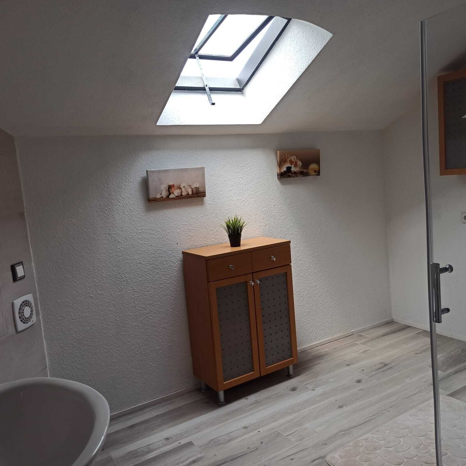 Une salle de bain dot ée d’un puits de lumière, d’un meuble en bois et d’une petite étagère où sont disposés des objets décoratifs.