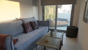 A modern living room with a grey sofa, striped pillows, a small table with a tray, and a sliding glass door leading to an outdoor area. - LOFT WITH PRIVATE TERRACE AND PARTHENON VIEWS (Athina)