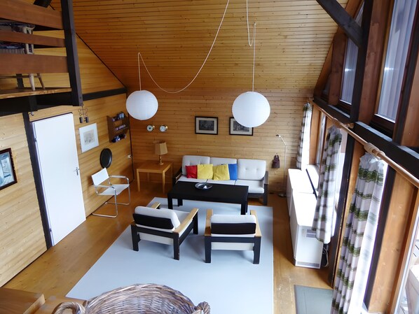 A modern interior with a wooden ceiling, a sofa set, a dining table, and a refrigerator.