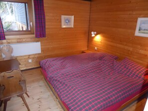A wooden-paneled room with a bed, a desk, and a window with curtains.